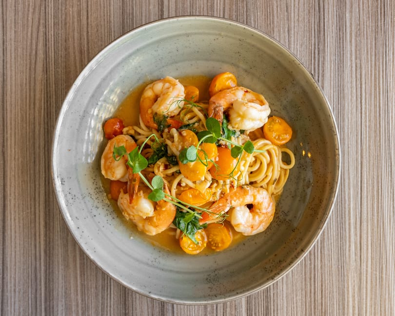 Shrimp scampi pasta with cherry tomatoes and fresh herbs in a gray bowl on a wooden table.