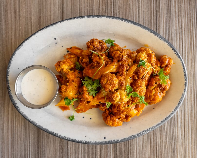 Crispy orange cauliflower florets with fresh parsley and a side of ranch dressing on a white plate.