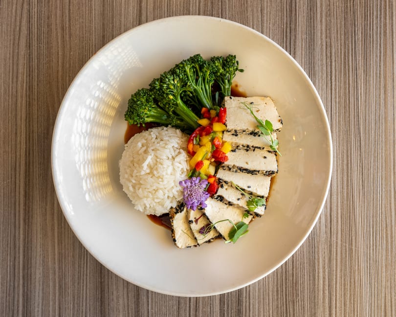 A white plate with sesame-crusted tofu, rice, broccolini, and colorful diced vegetables.