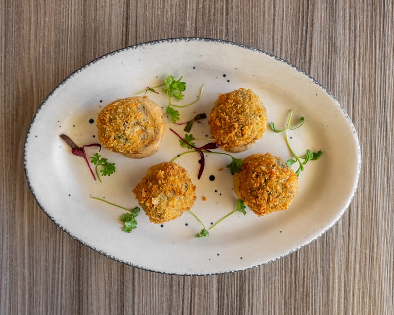Four breaded croquettes with sauce and herbs on an oval white plate.