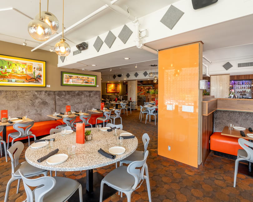 A vibrant restaurant interior with orange booths, modern gray chairs, and colorful artwork on the walls.