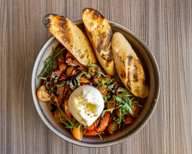 Burrata cheese with tomatoes, arugula, balsamic glaze, and toasted bread slices in a bowl.