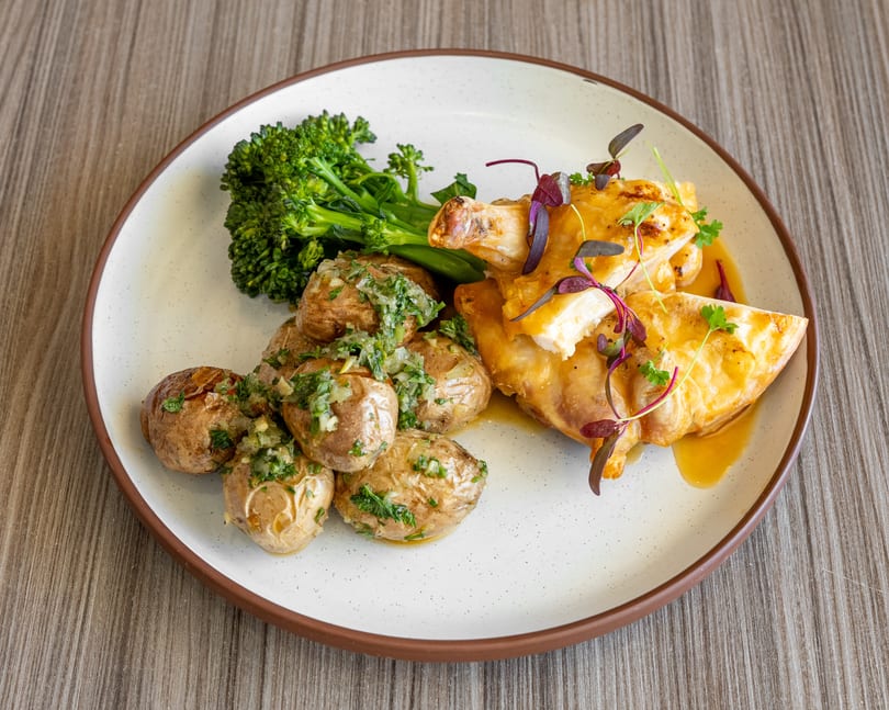 Roasted chicken with crispy skin, baby potatoes with herbs, and steamed broccoli on a white plate.