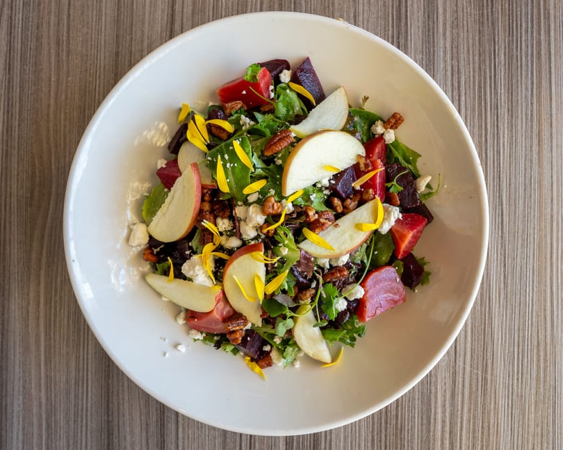 Overhead view of a vibrant salad with mixed greens, beets, apples, pecans, feta, and yellow petals.